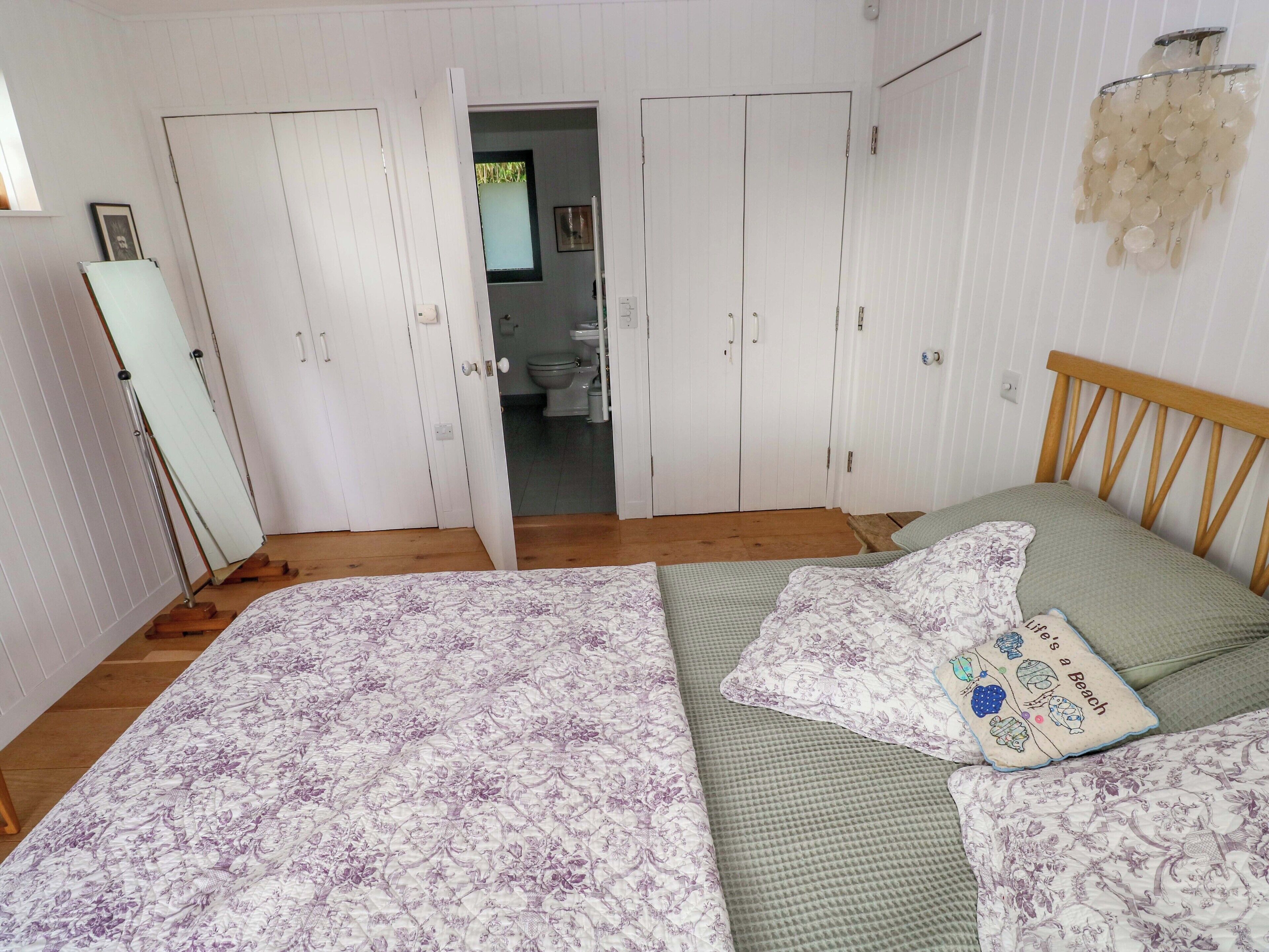 Ein Schlafzimmer mit Bett, Nachttisch, Kleiderschrank und einem durchgegangenen Tür angedeuteten Badezimmer.