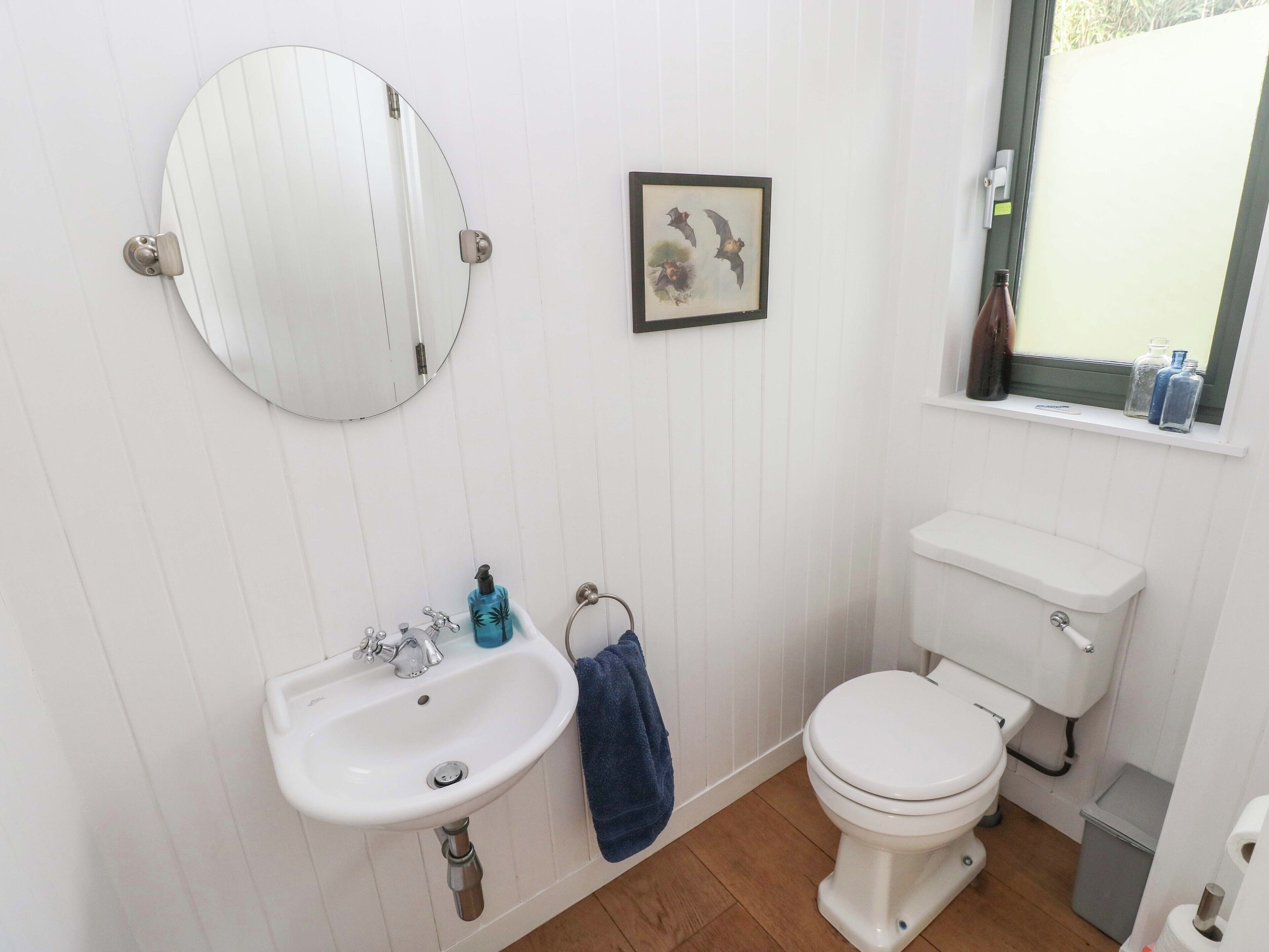 Un baño con un lavabo blanco, un inodoro, un espejo y una ventana con botellas en el alféizar.