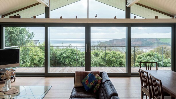 A spacious living area with a large window overlooking a scenic landscape, a leather sofa, and a dining table with chairs. - Green Shutters (Pembroke)