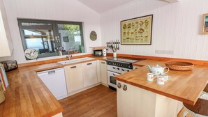 A compact kitchen with wooden countertops, white cabinetry, a stove, and a sink. - Green Shutters (Pembroke)