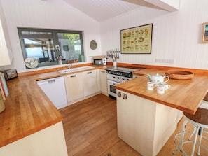 A compact kitchen with wooden countertops, white cabinetry, a stove, and a sink. - Green Shutters (Pembroke)
