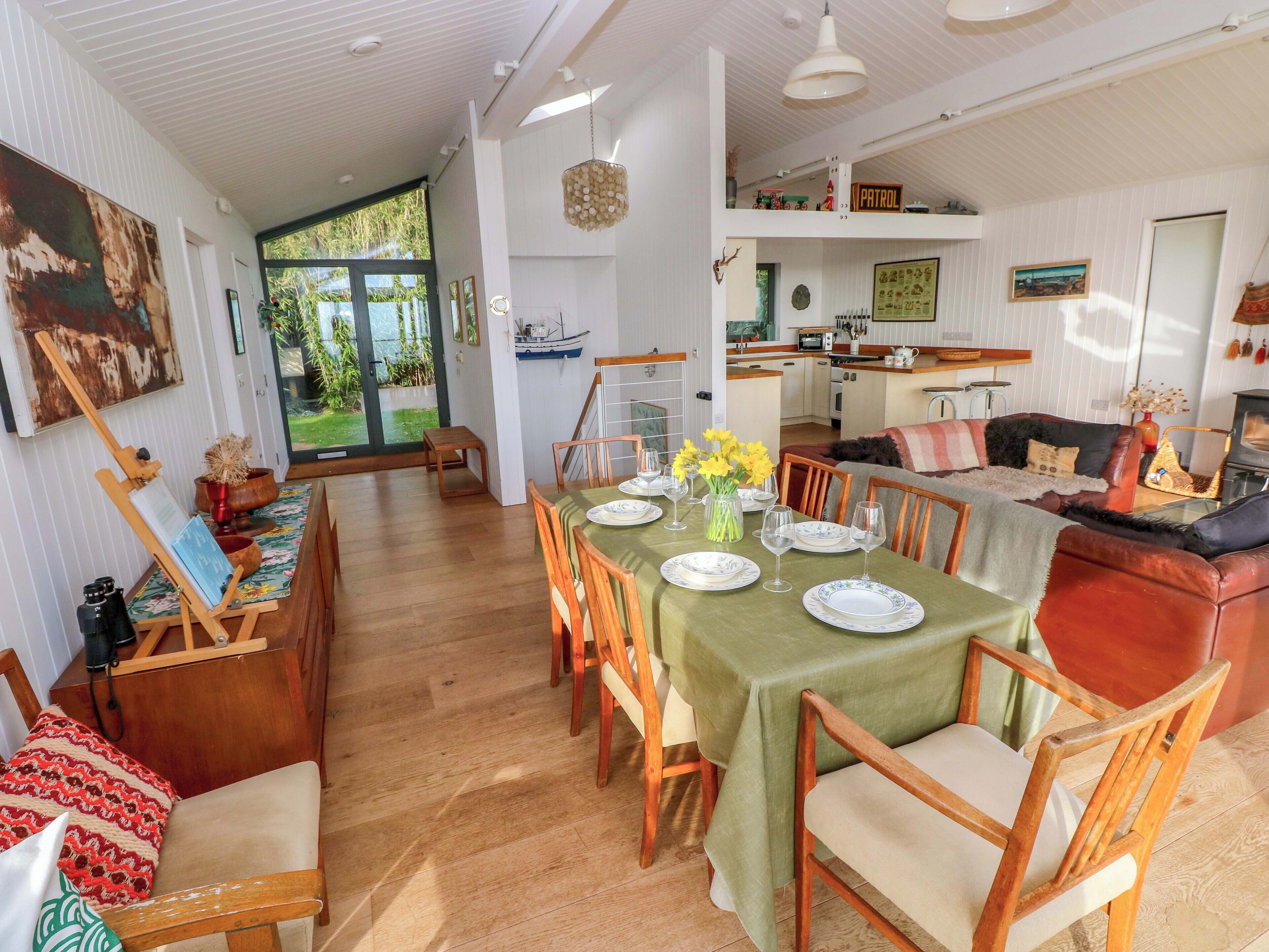 A spacious living area with a dining table set for six, a cozy seating area with a sofa, and a kitchen in the background.