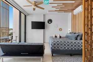 Ein modernes Schlafzimmer mit Bett, Sofa, Deckenventilator, Fernseher und Fenster.