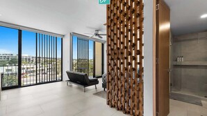 Amplia habitación con ventanas grandes, un separador de madera moderno, ventilador de techo y vista a la ciudad.