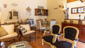 A cozy living room with a sofa, chairs, a coffee table, and a television. There is a wooden cabinet with glass doors and a decorative mirror on the wall. - Casa com Piscina e rea Gourmet em Boi Ucanga (São Sebastião)