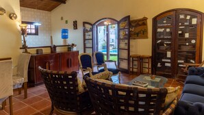 A cozy living room with wicker furniture, a glass coffee table, and a view through a glass door to the outside. - Casa com Piscina e rea Gourmet em Boi Ucanga (São Sebastião)