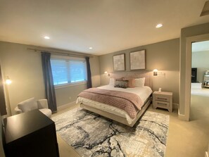 Une chambre à coucher comprenant un lit, des tables de chevet, un bureau, une chaise, une fenêtre avec des rideaux et des œuvres d’art accrochées au mur.