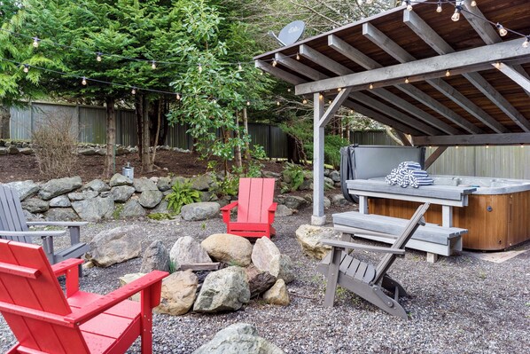 Une terrasse extérieure dotée d’une pergola en bois, d’un jacuzzi et de fauteuils Adirondack.