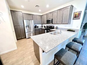 Una cocina moderna con encimeras de granito, electrodomésticos de acero inoxidable y una zona de bar con taburetes.