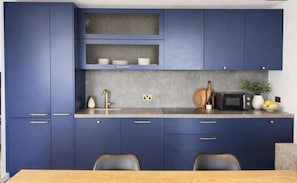 A modern kitchen with blue cabinets, a granite countertop, a microwave, and a dining area with a table and chairs. - Canary wharf iconic London skyline view (London)