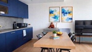 A modern kitchen with blue cabinets, a wooden dining table, and a flat-screen TV. - Canary wharf iconic London skyline view (London)