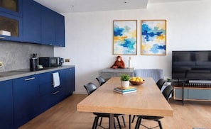 A modern kitchen with blue cabinets, a wooden dining table, and a flat-screen TV. - Canary wharf iconic London skyline view (London)