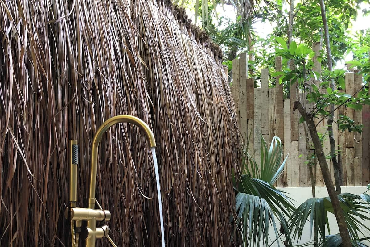 A hot tub with a thatched roof backdrop, surrounded by greenery.