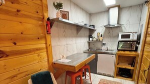 Uma cozinha compacta com paredes de madeira, área de refeições com mesa e cadeiras, e um forno de micro-ondas.