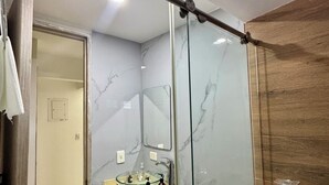 Ein modernes Badezimmer mit einer Duschkabine aus Glas, einer Wand mit Marmorplatten und einer Holzvertäfelung an einer Seite.
