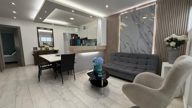 Ein modernes Wohnzimmer mit einem grauen Sofa, einem runden Couchtisch und einem Essbereich mit weißem Tisch und Stühlen.