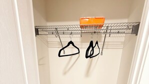 A walk-in closet with a metal rack holding two black hangers and an orange basket. - The Luxe Haven - Stylish 2BR | 2BA Retreat •Comfort • Privacy  • Perfect Location (Calgary)