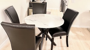 A dining area with a round table and four chairs, a kitchen in the background, and a light wooden floor. - The Luxe Haven - Stylish 2BR | 2BA Retreat •Comfort • Privacy • Perfect Location (Calgary)