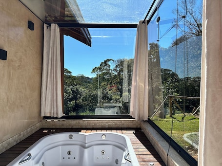 A modern bathroom with a glass-enclosed window, a wooden floor, and a white bathtub.
