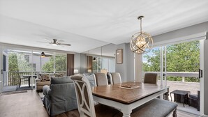 A spacious dining area with a wooden table and chairs, large windows, and a ceiling fan.