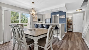 A modern kitchen with white cabinetry, a central island, and a dining area with a table and chairs.