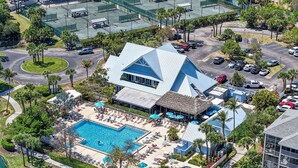 An aerial view of a resort with a large pool, lounge areas, and a thatched-roof building.
