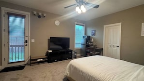 Ein Schlafzimmer mit Bett, Fernseher, Deckenventilator und einer Tür mit Fenster.