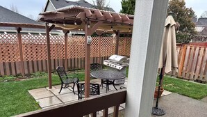 Eine Terrasse mit einer Pergola, einem Grill und Gartenmöbeln.