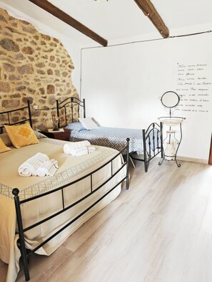 A bedroom with a stone wall, a bed with a metal frame, a nightstand, a lamp, and a wall-mounted mirror. - Locanda Jannas (Orgosolo)