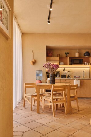 A modern kitchen with wooden cabinets, a dining table with chairs, a hanging light fixture, and a vase with flowers. - Casona Xochimilco - Carmen (Oaxaca de Juárez)