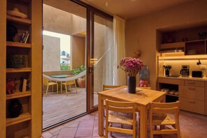 A compact kitchen with wooden cabinets, a dining table with chairs, a small island with a sink, and a view through a glass door to an outdoor area with a hammock and chairs. - Casona Xochimilco - Carmen (Oaxaca de Juárez)