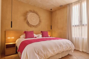 A bedroom with a large bed, a nightstand, a wall-mounted circular decor, and a window with curtains. - Casona Xochimilco - Carmen (Oaxaca de Juárez)
