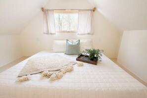 A bedroom with a large bed, a window with curtains, and a small plant on a bedside table.