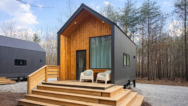 Una baita moderna con facciata in legno, un portico con gradini e due sedie.