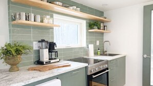 Una cucina moderna con mobili verdi, forno a incasso, macchina da caffè e mensole in legno.