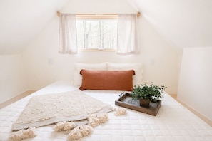 A bedroom with a bed, a window with curtains, a bedside plant, and a decorative tray.
