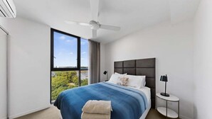 A modern hotel room with a large bed, a ceiling fan, a nightstand, and a window with a city view.