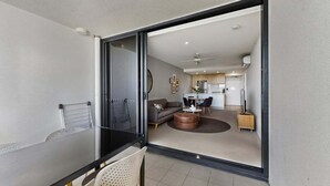 A modern living room with a glass partition, a dining area with a table and chairs, and a kitchen in the background.