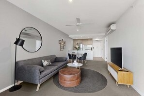 A modern living room with a grey sofa, round coffee table, and a flat-screen TV on a wooden stand. - Hamilton Portside Luxe – Level 5 (Brisbane)
