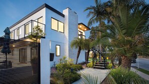 A modern two-story house with a balcony, a staircase, and a well-maintained garden with palm trees and shrubs. - Seal Beach Escape by Avantstay Modern Home + Fireplace Prvte Courtyard + Walk to Beach + Dining (Seal Beach)
