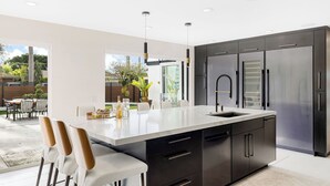 A modern kitchen with a large island, stainless steel appliances, and a dining area with outdoor seating. - Seal Beach Escape by Avantstay Modern Home + Fireplace Prvte Courtyard + Walk to Beach + Dining (Seal Beach)