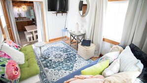 A room with a bed, a sofa, a small table, a TV, and a window with curtains. - Pet-Friendly Coastal Cottage • Walk to Pier (Old Orchard Beach)