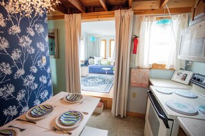 Une cuisine équipée d’une cuisinière, une table à manger dressée avec de l’assiette, et une vue sur le salon par une porte ouverte.