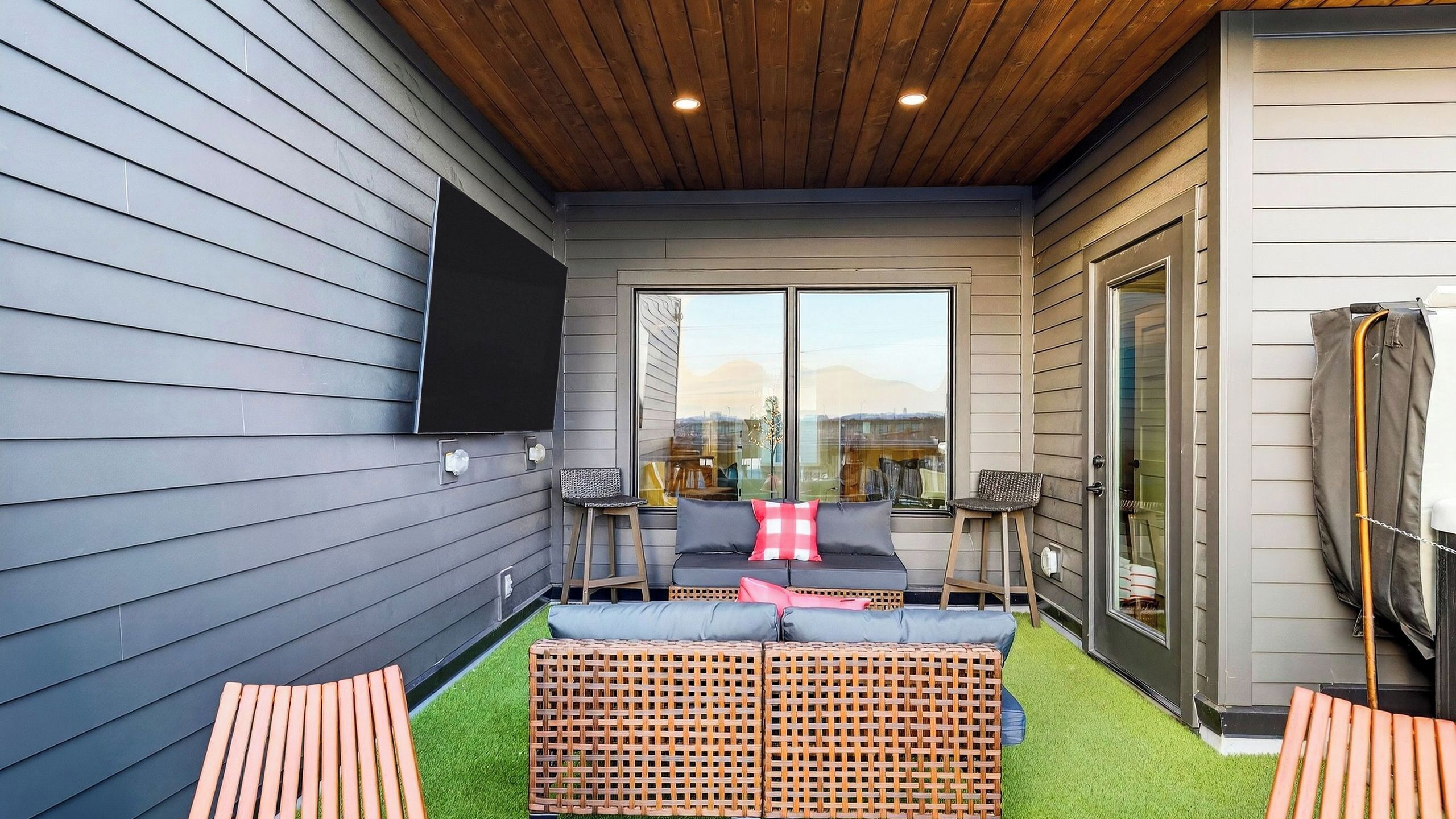 A covered outdoor seating area with a sofa, chairs, and a TV mounted on the wall.