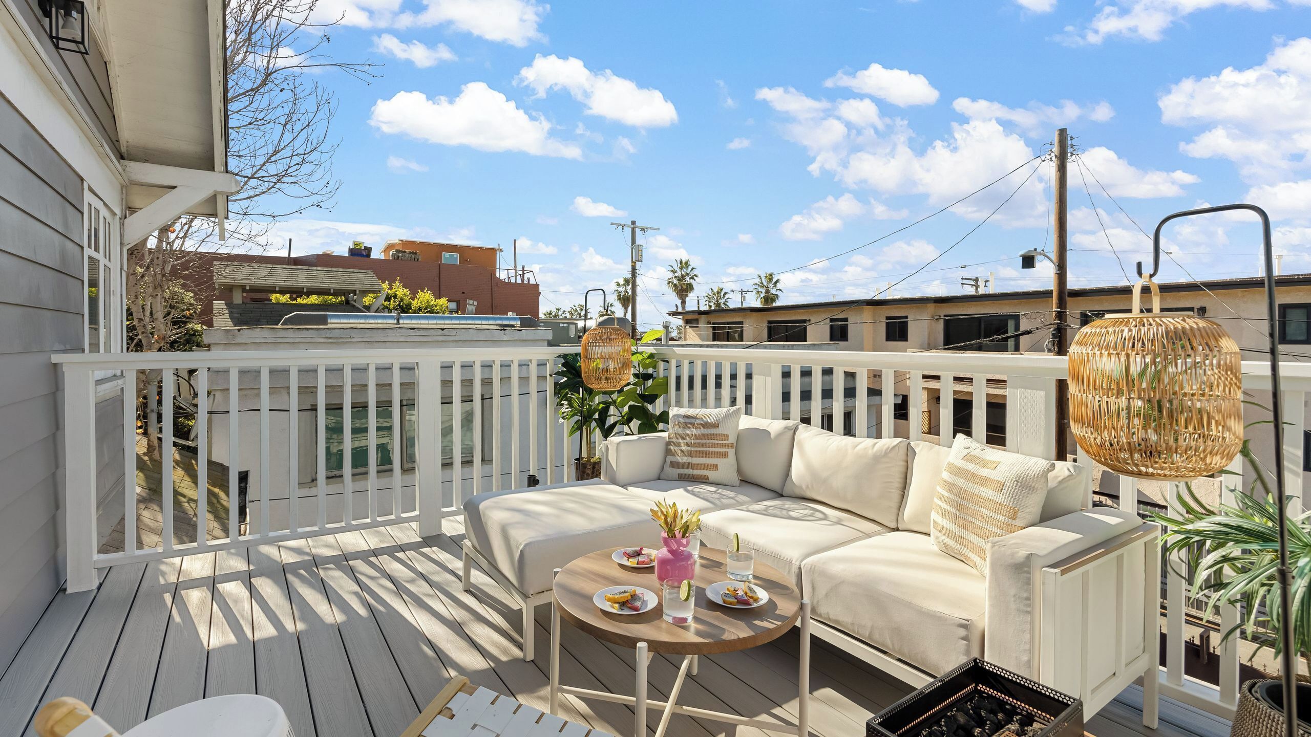 A deck with a white railing, a beige sofa, and a round wooden table with plates and drinks.