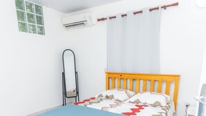 A bedroom with a bed, a mirror, an air conditioning unit, and a window. - Appartement Standard a Cayenne Baduel (Cayenne)