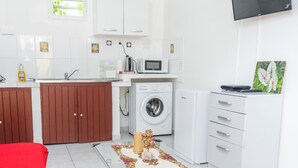 A modern kitchen with white cabinets, a washing machine, and a flat-screen TV. - Appartement Standard a Cayenne Baduel (Cayenne)