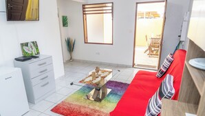 A modern living room with a red sofa, a small white desk, a colorful rug, and a large window. - Appartement Standard a Cayenne Baduel (Cayenne)