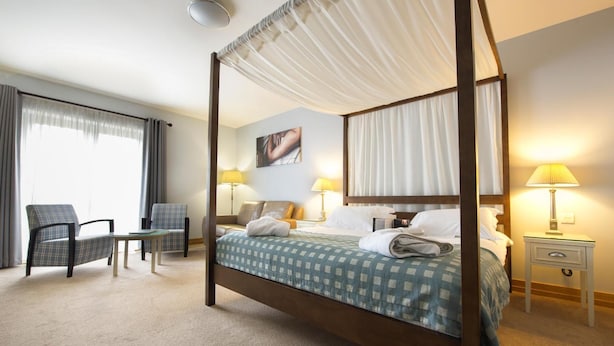 A four-poster bed with a checkered bedspread, two bedside tables with lamps, a chair, and a small table. - Bicester Country Club (Bicester)