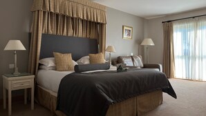 A hotel room with a large bed, two bedside tables, a headboard, and a window with curtains. - Bicester Country Club (Bicester)